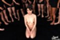 Kneeling naked hands resting on her thighs surrounded by men